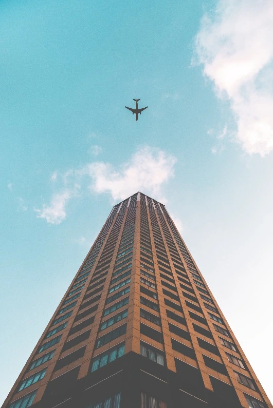 Photo of an airplane above a skyscraper with clouds